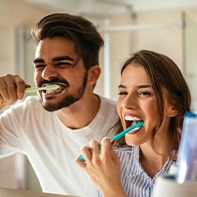 Couple smiling while brushing teeth in bathroom
