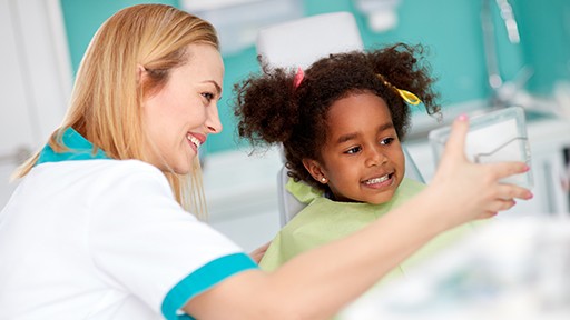 Dentist showing little girl who smile in mirror