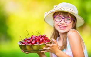 young person with braces holding a bowl of cherries