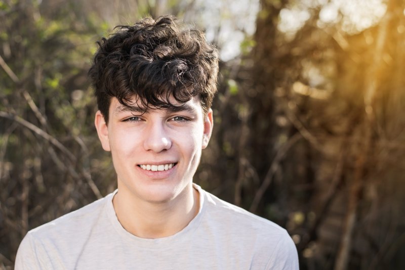 a young teenage boy standing outside and smiling after having his braces removed