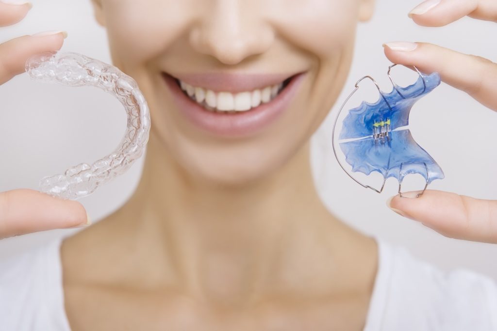 Smiling woman holding up different types of retainers