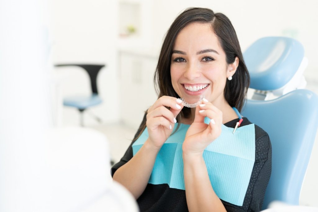Adult patient smiling while holding clear aligner
