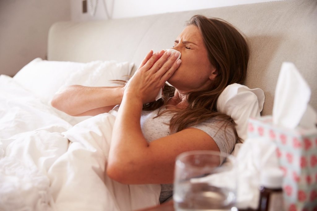 Woman blowing her nose while lying in bed